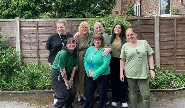 A group of smiling females dressed in green stand together 