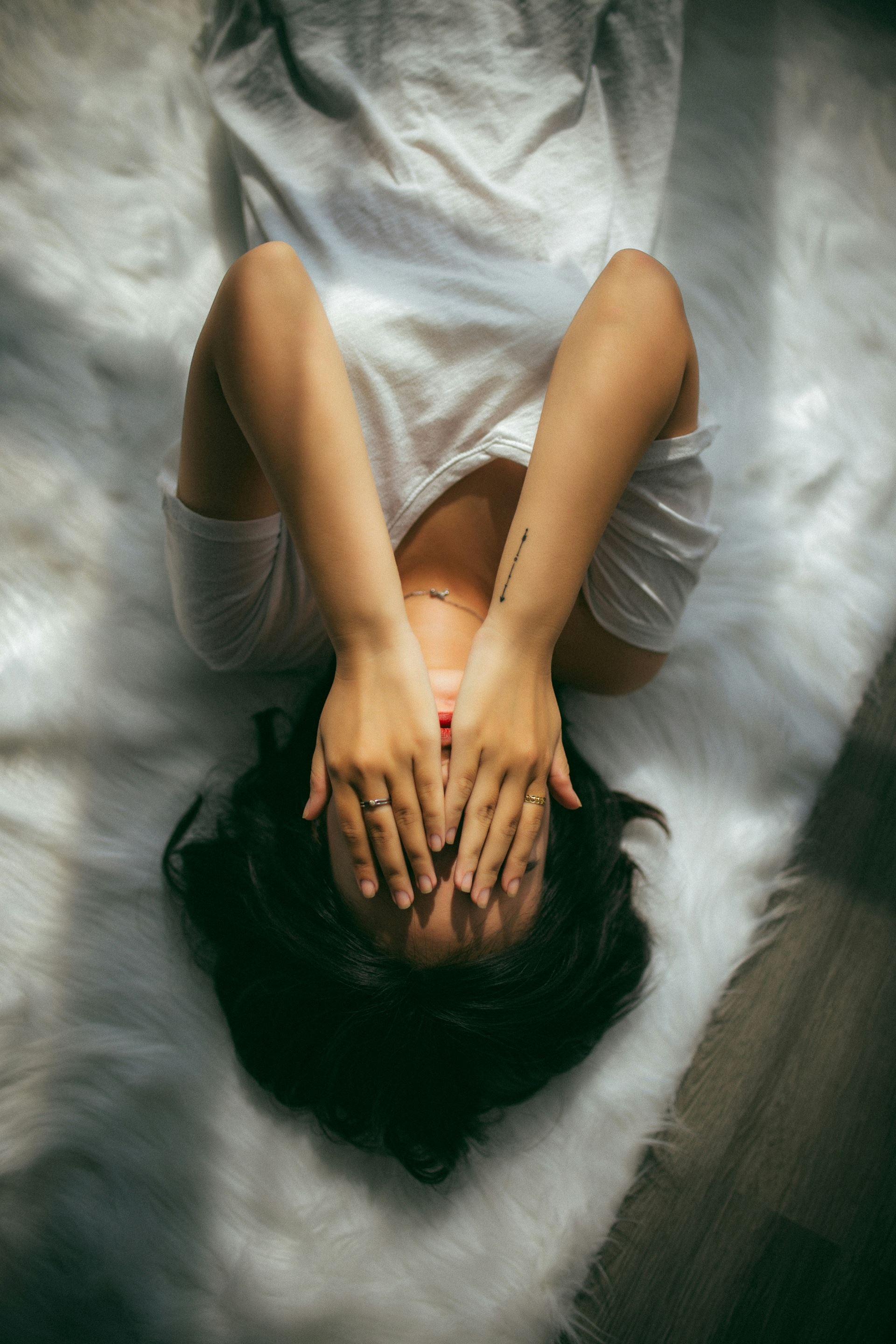 A person lying down with their hands over their face