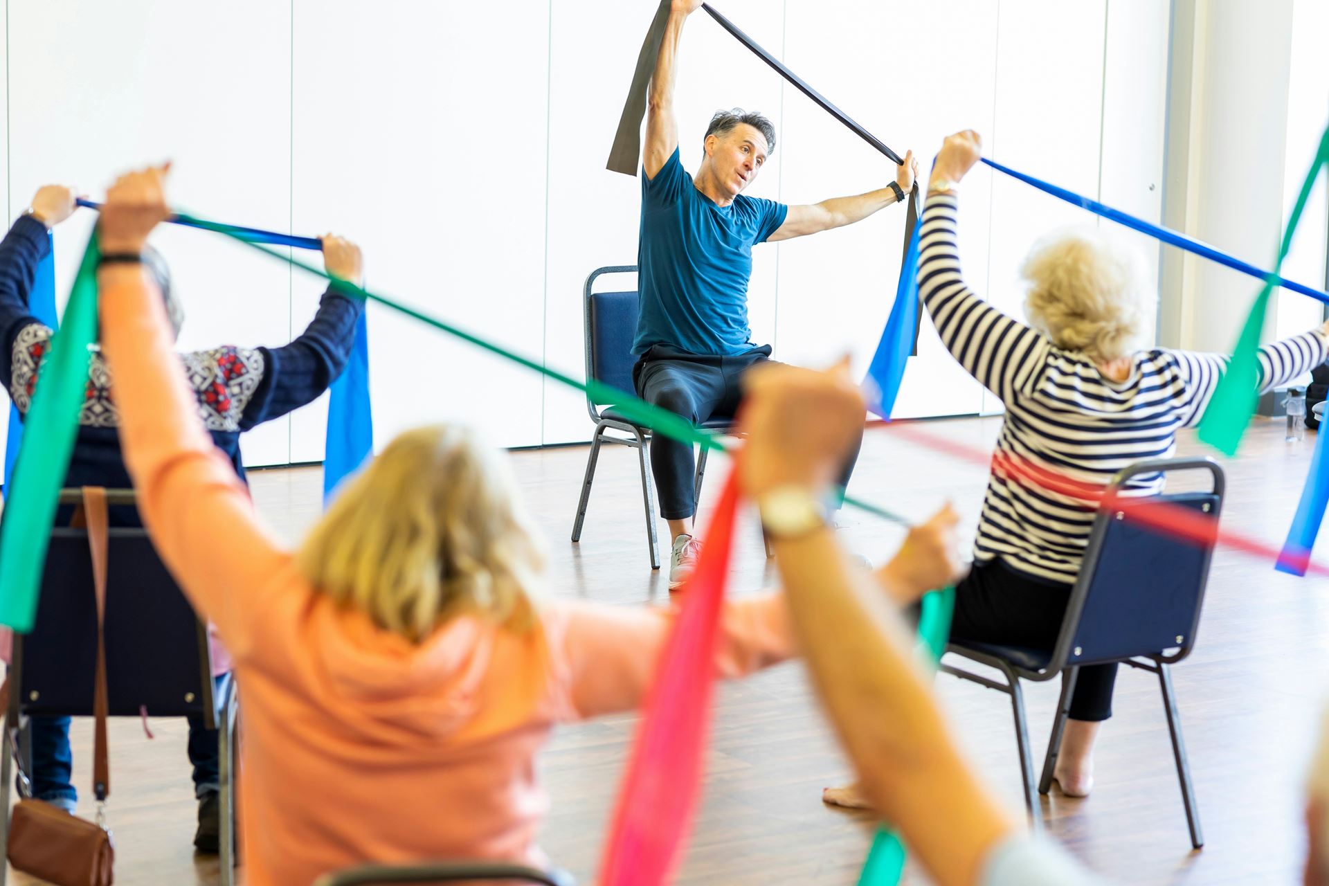 A group of people holding coloured ribbons copy the instructor at the front